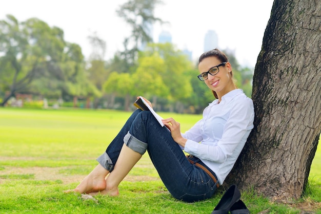 Junge Studentin, die ein Buch liest und im Park studiert