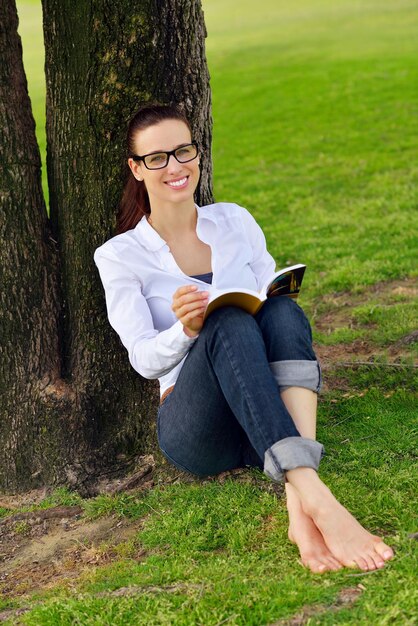 Junge Studentin, die ein Buch liest und im Park studiert