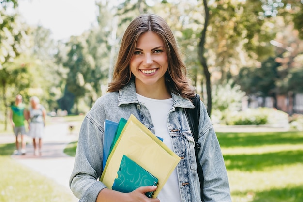 Junge Studentin, die im Park lächelt. Nette Studentin hält Ordner und Notizbücher in den Händen. Lernen, Bildungskonzept