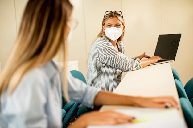 Junge Studentin, die medizinische Gesichtsschutzmaske für Virenschutz am Hörsaal trägt