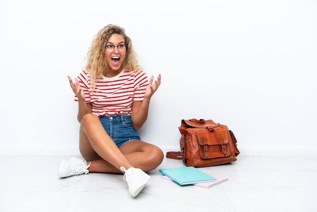 Junge Studentin, die mit überraschtem Gesichtsausdruck auf dem Boden sitzt