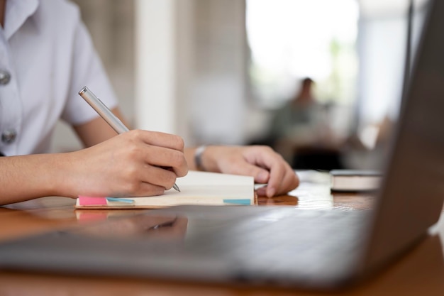 Junge Studentin, die online auf einem Notebook schreibt, lernt über einen Laptop, der in der Bibliothek sitzt