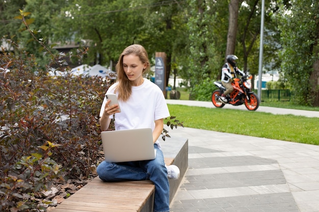Junge Studentin, die während der Zeit zum E-Learning im Park auf der Bank mobile SMS-Nachrichten sendet