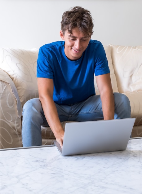 Junge Studentin, die zu Hause auf dem Sofa lächelt, in intelligenter Arbeit mit College-Klassen und Unterricht verwendet Laptop