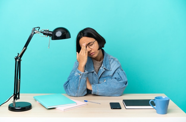 Junge Studentin gemischte Rasse, die auf einem Tisch mit Kopfschmerzen studiert