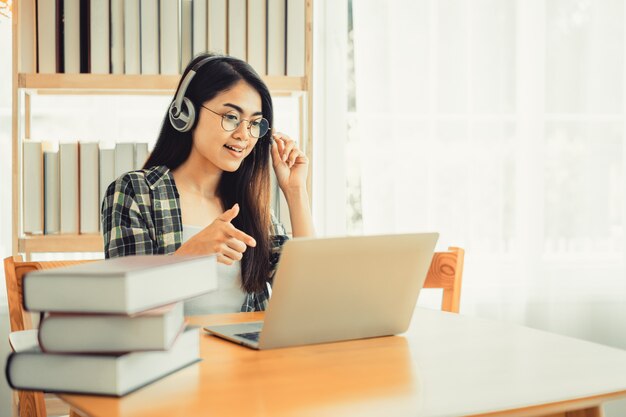 Junge Studentin im karierten Hemd sitzt am Tisch mit Laptop beim Lernen.