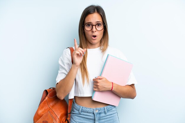 Junge Studentin isoliert auf blauem Hintergrund, die beabsichtigt, die Lösung zu realisieren, während sie einen Finger nach oben hebt