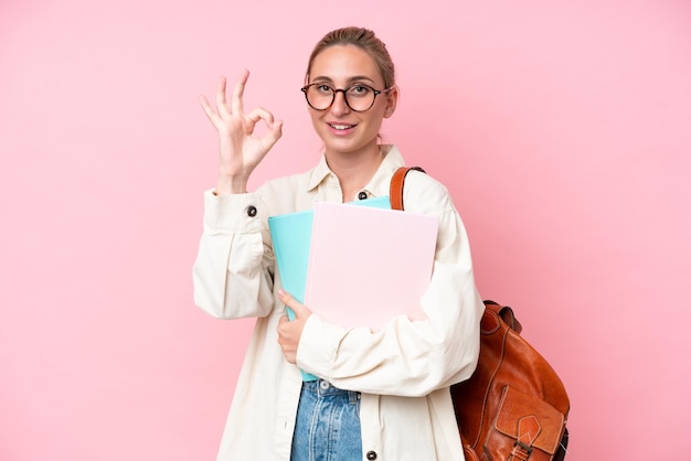 Junge studentin, kaukasische frau isoliert auf rosa hintergrund, die ok-zeichen mit den fingern zeigt