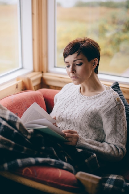 Junge Studentin liest ein Buch in einer gemütlichen Atmosphäre zu Hause. Fernlernkonzept.