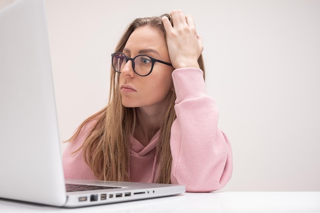 Junge Studentin mit Brille, die zu Hause auf den Laptop schaut, fühlt sich gestresst und frustriert