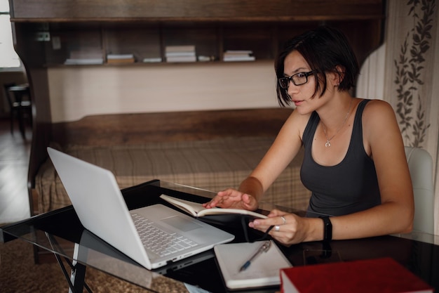 Junge Studentin mit Brille und Laptop kommuniziert im Internet mit Lehrern