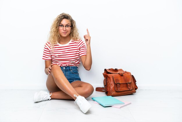 Junge Studentin sitzt auf dem Boden und zeigt mit dem Zeigefinger auf eine tolle Idee