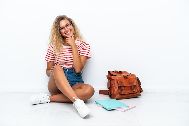 Junge Studentin sitzt lächelnd auf dem Boden