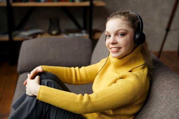 Junge Studentin studiert im Wohnzimmer, sitzt auf dem Sofa und benutzt Kopfhörer