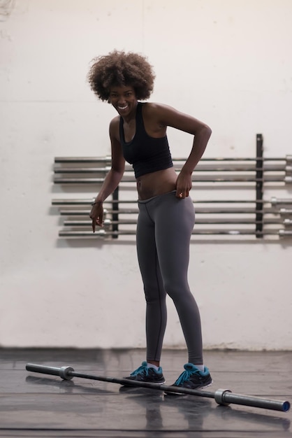 Junge süße afrikanisch-amerikanische Sportlerin im Fitnessraum, die leere Stangen hebt
