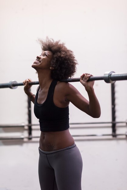 Junge süße afrikanisch-amerikanische Sportlerin im Fitnessraum, die leere Stangen hebt