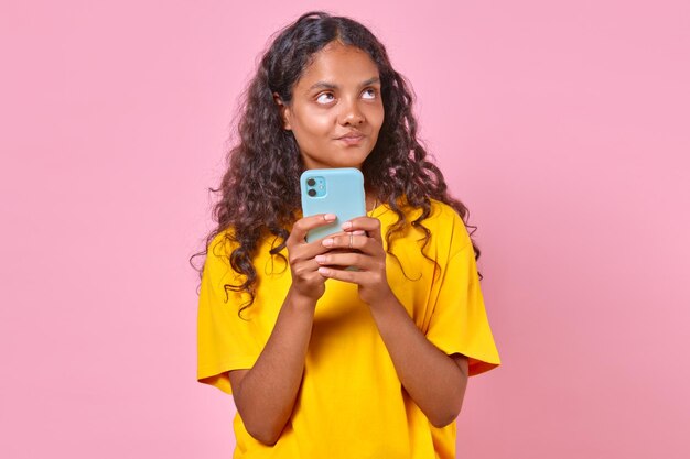 Junge, süße indische Teenager-Frau sieht träumerisch auf und hält das Telefon in der Hand