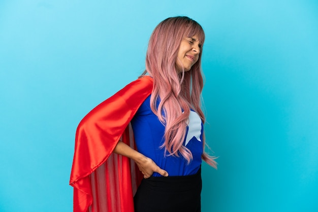 Junge Superheldin mit rosa Haaren isoliert auf blauem Hintergrund, die an Rückenschmerzen leidet, weil sie sich angestrengt hat