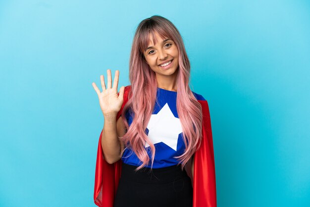 Junge Superheldin mit rosa Haaren isoliert auf blauem Hintergrund, die fünf mit den Fingern zählt
