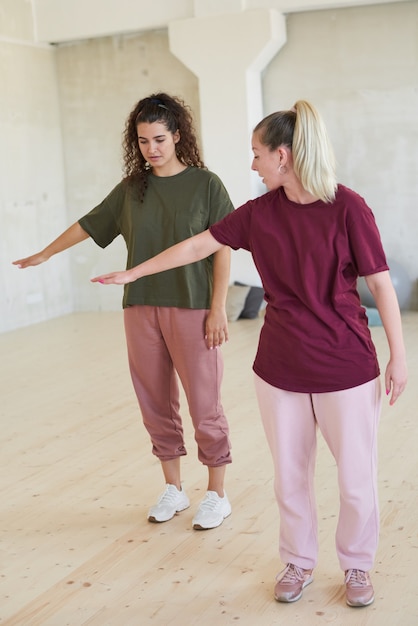 Junge Tanzlehrerin, die der Frau die Bewegung zeigt und ihr das Tanzen im Studio beibringt