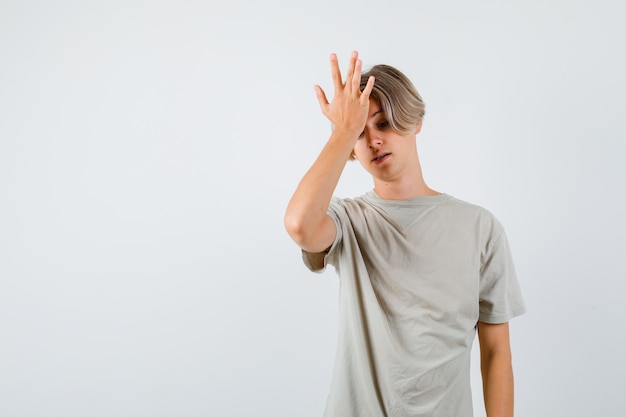 Junge teenager, die hand auf der stirn im t-shirt halten und vergesslich aussehen, vorderansicht.