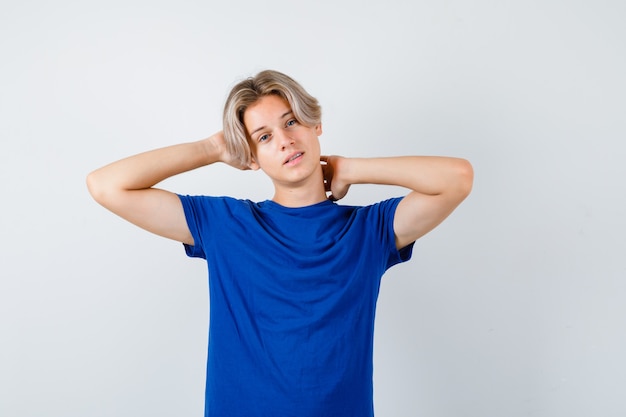 Junge Teenager im blauen T-Shirt mit Händen hinter Kopf und Nacken und zögernd, Vorderansicht.