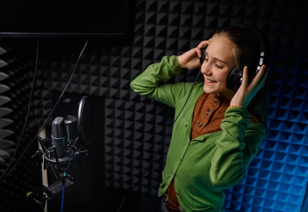 Junge Teenager-Sängerin mit Kopfhörern singt neues Lied mit Mikrofon im Plattenstudio