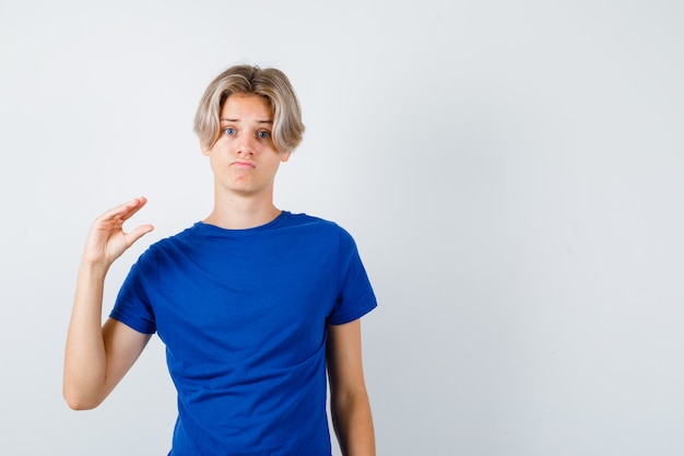 Foto junge teenager zeigen kleine schild in blauem t-shirt und suchen düster, vorderansicht.