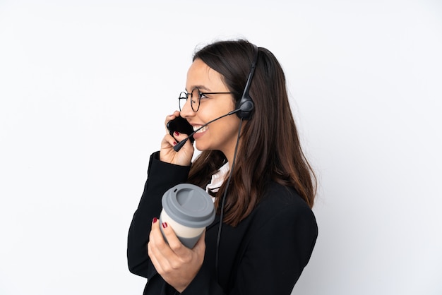 Junge Telemarketerfrau auf weißer Wand, die Kaffee hält, um und ein Handy wegzunehmen