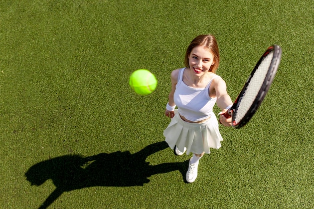 Junge Tennisspielerin in weißer Sportuniform spielt Tennis auf einem grünen Platz, weibliche Trainerin mit Tennis