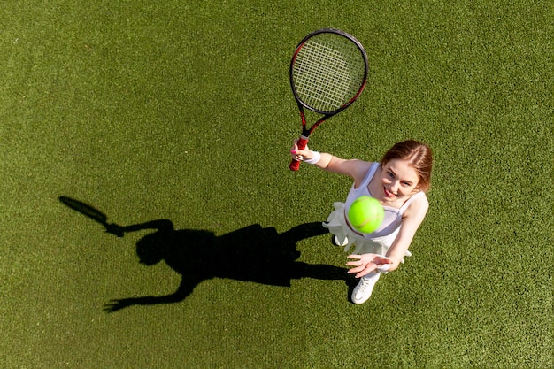 Junge Tennisspielerin in weißer Sportuniform spielt Tennis auf grünem Platz