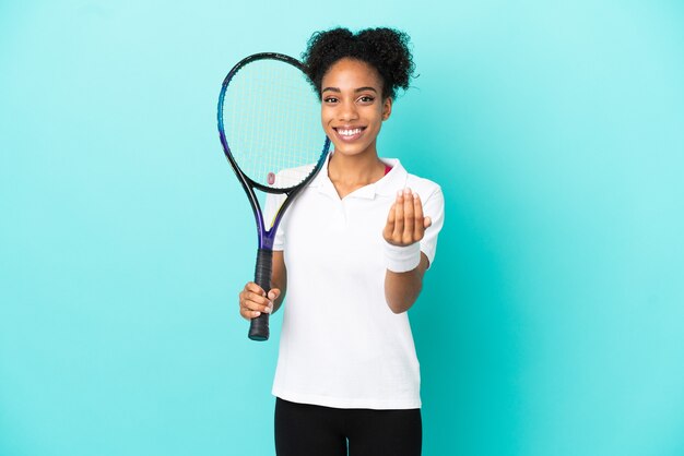 Junge Tennisspielerin isoliert auf blauem Hintergrund, die einlädt, mit der Hand zu kommen. Schön, dass du gekommen bist