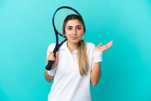 Junge Tennisspielerin isoliert auf blauem Hintergrund, die Zweifel hat, während sie die Hände hebt