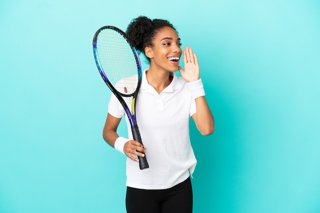 Junge Tennisspielerin isoliert auf blauem Hintergrund schreien mit weit geöffnetem Mund zur Seite