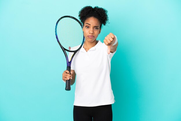 Junge Tennisspielerin isoliert auf blauem Hintergrund zeigt Daumen nach unten mit negativem Ausdruck