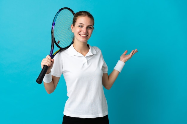 Junge Tennisspielerin lokalisiert auf blauer Wand, die Hände zur Seite für Einladung zum Kommen ausdehnt