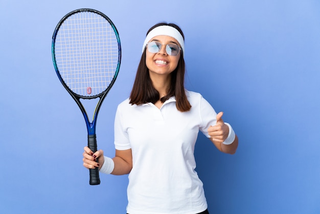 Junge Tennisspielerin über der Wand, die imaginären Copyspace auf der Handfläche hält, um eine Anzeige und mit den Daumen nach oben einzufügen