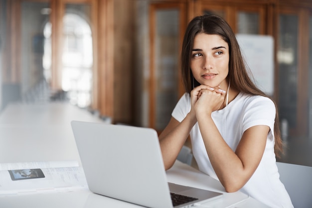 Junge Texterin, die einen Notebook-Computer verwendet, um einen Artikel zu schreiben, der über die Veröffentlichung eines neuen Buches oder einer Zeitschrift nachdenkt.