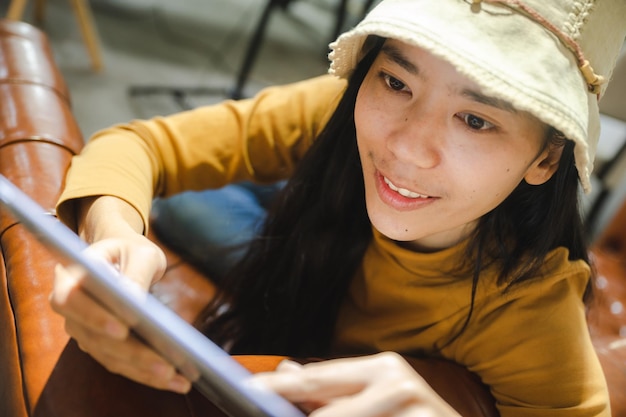 Foto junge thailändische asiatin, die auf einem schlafsofa liegt und ein digitales computertablett verwendet, um sich zu entspannen und online zu arbeiten