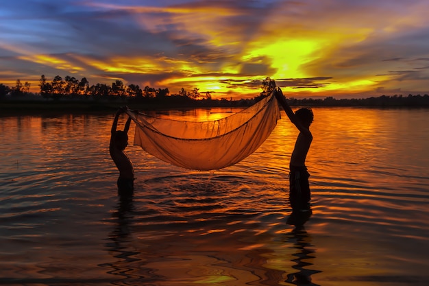 Junge thailändische Fischer, die nach Fischen im Sonnenuntergang suchen.