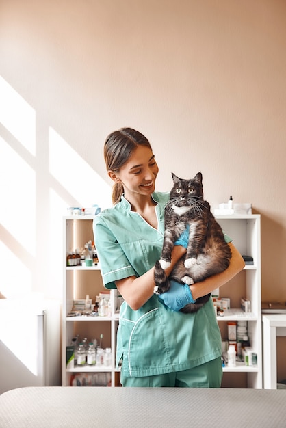 junge Tierärztin, die eine große schwarze Katze hält und in der Klinik lächelt