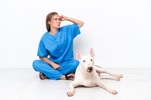 Junge Tierarzt-Engländerin, die auf dem Boden sitzt, mit Hund, der Zweifel hat und mit verwirrendem Gesichtsausdruck