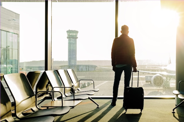 Junge Touristen mit einem Koffer stehen in der Nähe des Fensters am Flughafen am frühen Morgen bei Sonnenlicht