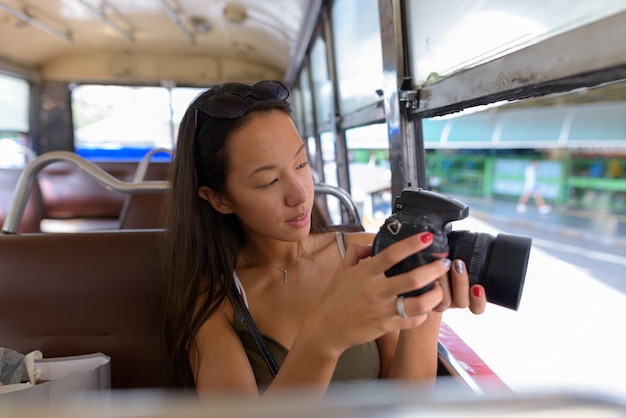 Junge Touristenfrau, die am Bus sitzt, während DSLR-Kamera verwendet