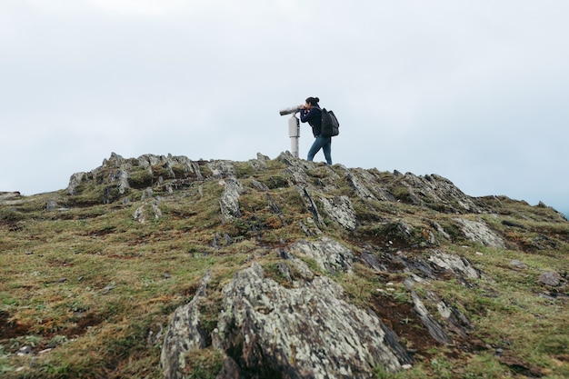 Junge Touristenfrau, die durch münzbetriebenes Hochleistungsfernglas auf den Kaukasus-Bergen, Kazbegi, Georgia schaut