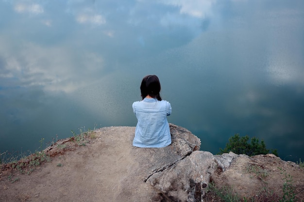 Junge Touristenfrau sitzt oben auf der Montierung und betrachtet eine schöne Landschaft. Wandernde Frau, die sich auf der Spitze der Klippe entspannt, genießt. attraktives Mädchen in Jeanskleidung