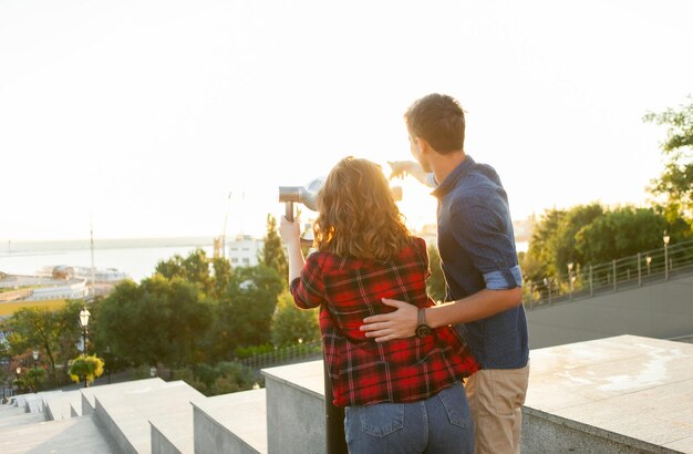 Junge Touristenpaare schauen bei Sonnenaufgang durch ein Stadtfernglas in der Stadt. Reisen, Urlaubskonzept