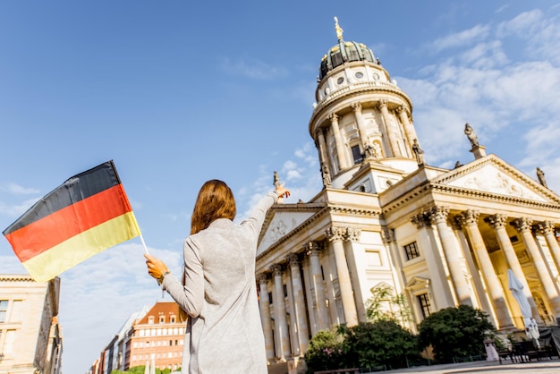 Junge Touristin, die mit deutscher Flagge auf dem Gendarmenplatz mit französischer Kirche und Oper im Hintergrund in Berlin steht?