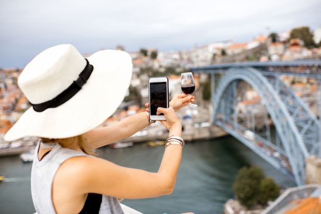 Junge Touristin fotografiert ein Glas Porto-Wein auf der Terrasse mit tollem Blick auf die Stadt Porto in Portugal