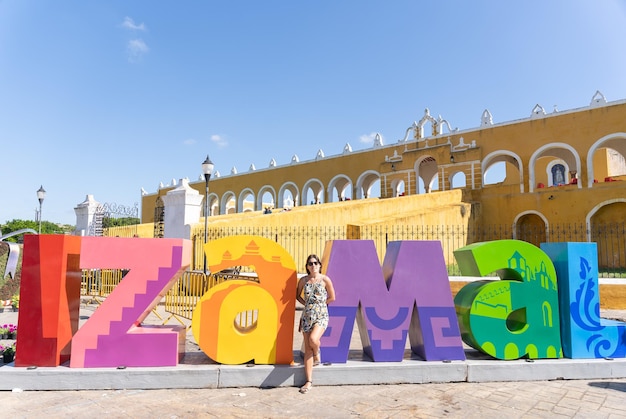 Junge Touristin macht ein Foto mit den bunten Buchstaben Izamal am Eingang des Klosters San Antonio in Mexiko